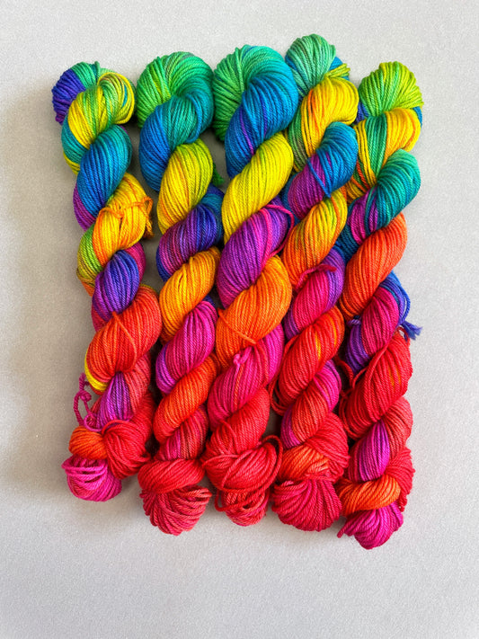 5 x 20g Hand-dyed Yarn mini skeins in colourway Bright Rainbow on our Sock/4ply Yarn base. The image shows the full skeins, twisted up and is on a Sock/4ply weight Yarn Base. The yarn contains 7 bright colours, sunshine, lava, ruby, apple, cyan, electric purple and neon pink and photographed on white background.