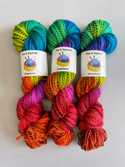 Full photo of 3 skeins of Hand-dyed Yarn in colourway Bright Rainbow on our Zebra DK yarn base. The yarn contains 7 bright colours, sunshine, lava, ruby, apple, cyan, electric purple and neon pink and is photographed on a white background. 