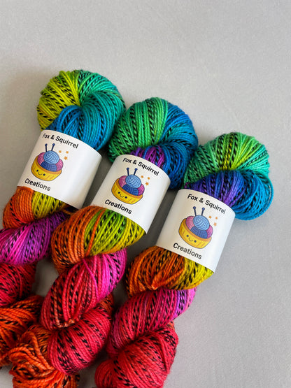 Close up shot of 3 skeins of Hand-dyed Yarn in colourway Bright Rainbow on our Zebra DK yarn base. The yarn contains 7 bright colours, sunshine, lava, ruby, apple, cyan, electric purple and neon pink and is photographed on a white background. 